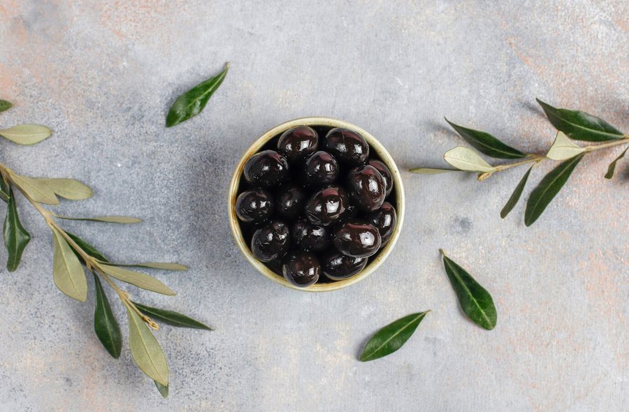 Bowl of black olives with olive leaves on a stone table