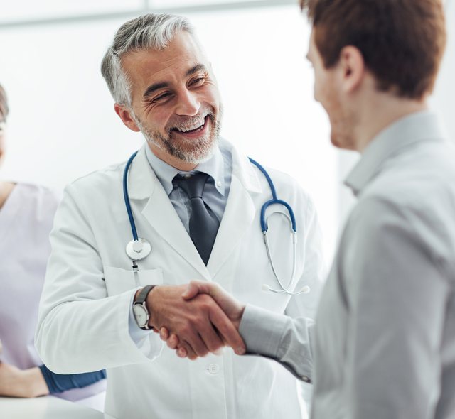 Smiling doctor shaking hands with a patient beside a nurse